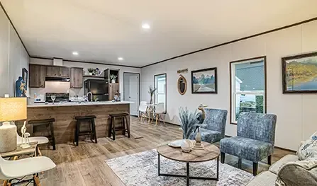 A modern Houston living room and open kitchen featuring wood flooring, blue chairs, a round coffee table, a wooden kitchen island with stools, and various wall decorations and paintings.