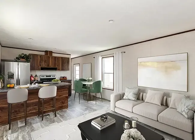 A modern open-concept living space by J Houston Zenith Properties featuring a kitchen with wood cabinets and stainless steel appliances, a dining area with a green table and chairs, and a seating area with a gray sofa and abstract artwork.