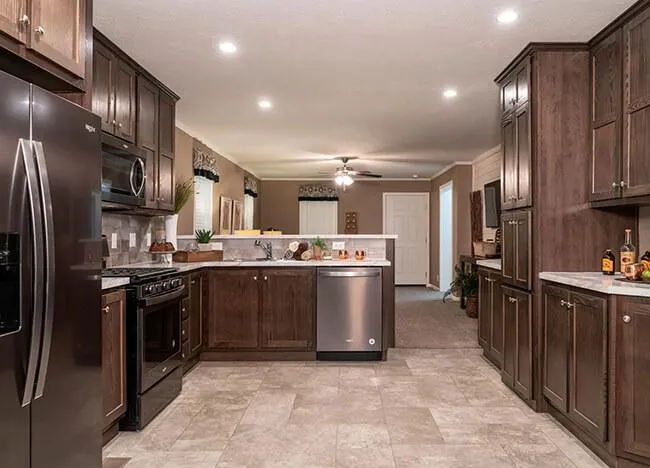 A modern kitchen with dark wood cabinets, stainless steel appliances, marble countertops, and tiled flooring. A ceiling fan and recessed lighting illuminate the room. This stylish culinary space by J Houston Properties is designed for both functionality and elegance.