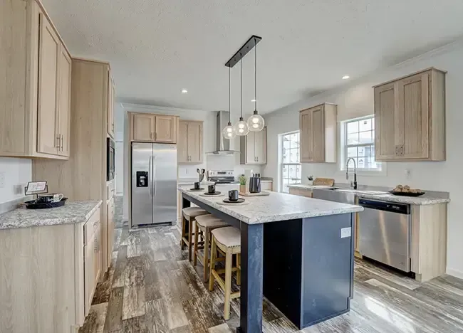 Modern kitchen with light wood cabinets, marble countertops, stainless steel appliances, center island with bar stools, and pendant lighting. Large windows provide natural light. This stunning space is brought to you by J Houston Properties.