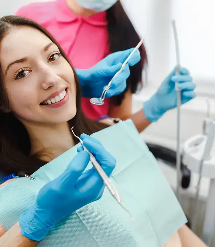 Smiling patient receiving a dental examination while a dentist uses dental instruments.