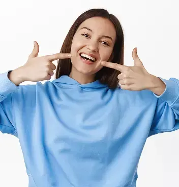 Smiling young woman pointing to her teeth with both hands, highlighting a healthy and confident smile.