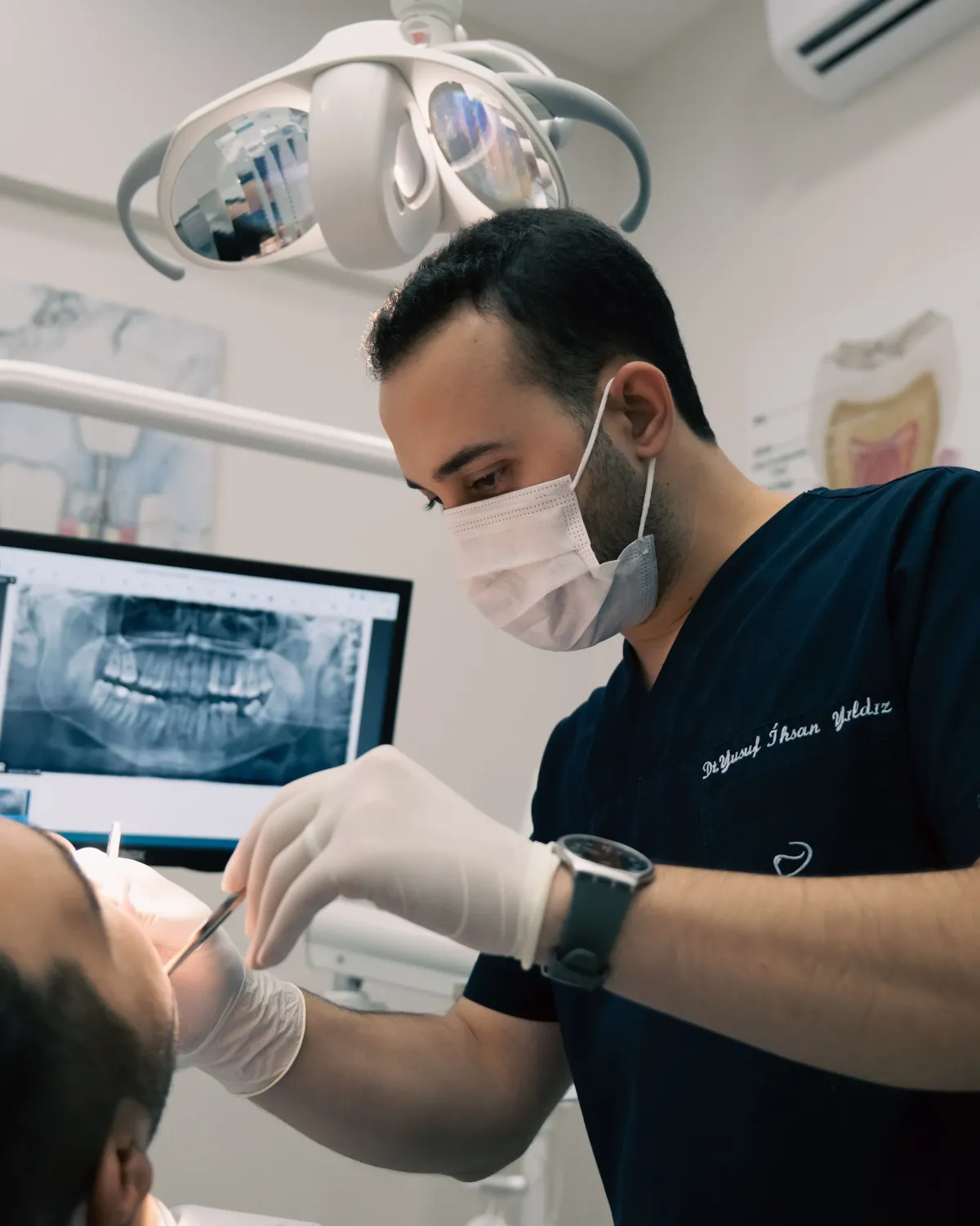 Dentist providing precise dental treatment to a patient in a modern clinic, with digital X-ray imaging visible in the background.