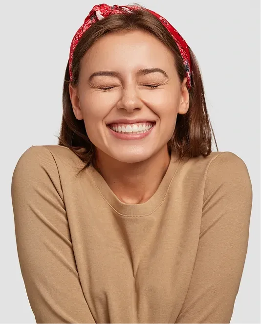 Smiling woman with her eyes closed, showing a bright and confident healthy smile.