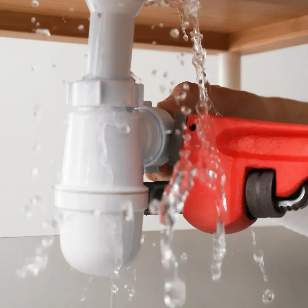 Plumber repairing leaking sink drain pipe during residential plumbing maintenance service by MMI Home Manager