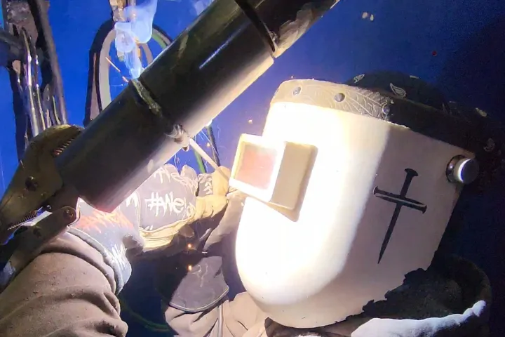 Welder in a workshop working on metal with sparks.