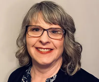 Woman with glasses smiling against a neutral background.