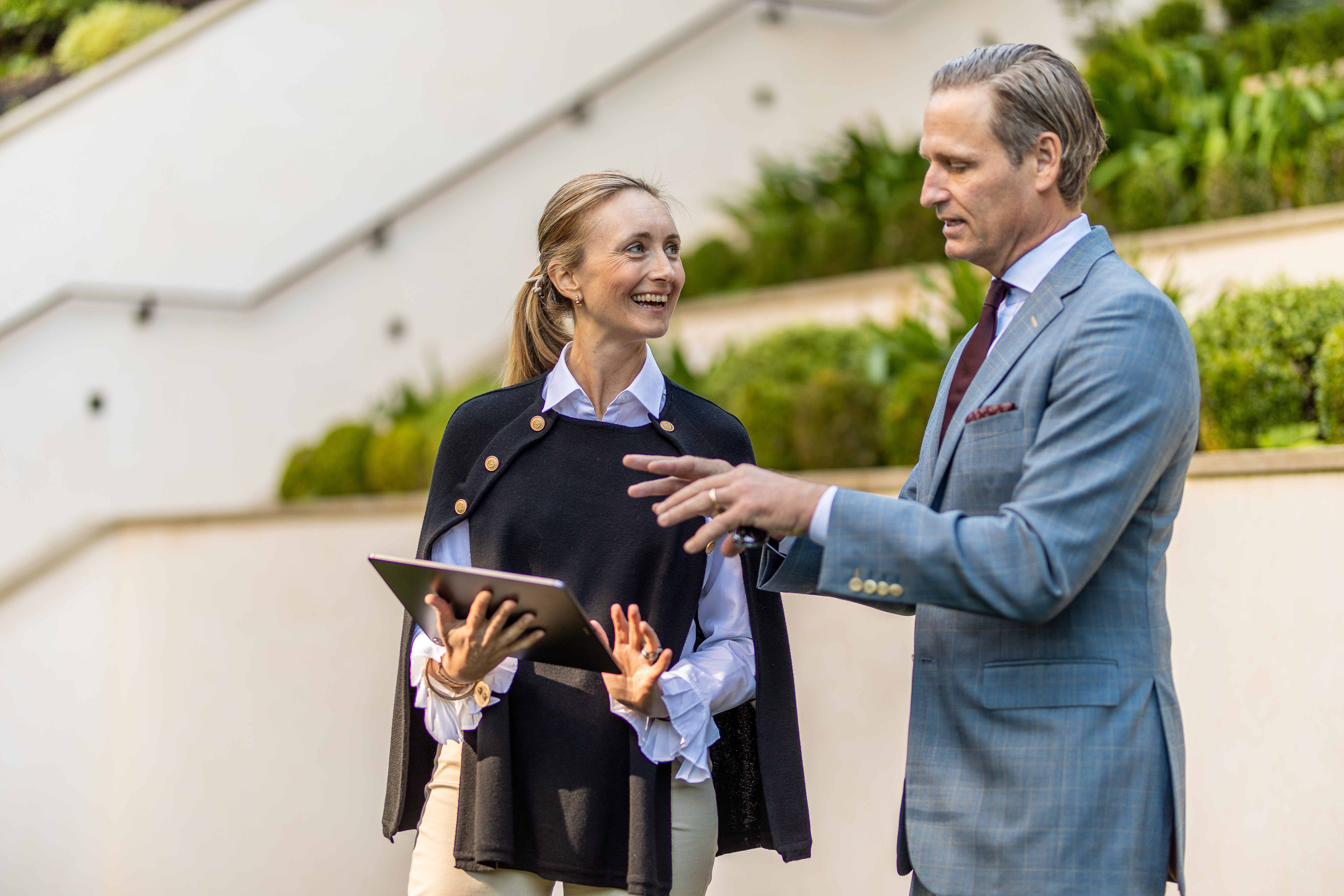 Two professionals discussing work outdoors with tablet, business collaboration and modern workplace