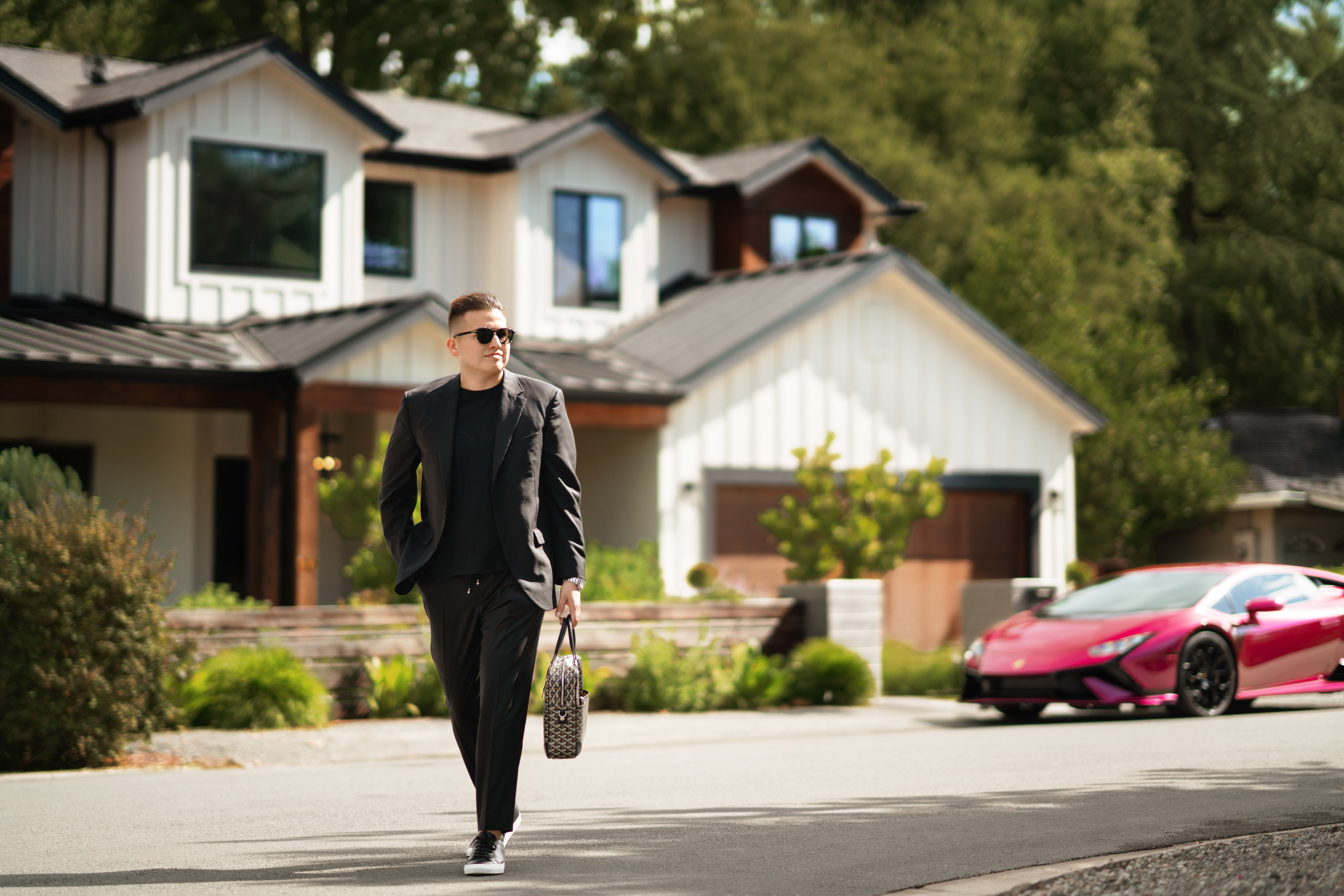 Man in stylish outfit walking in front of modern luxury home with sports car, upscale lifestyle scene