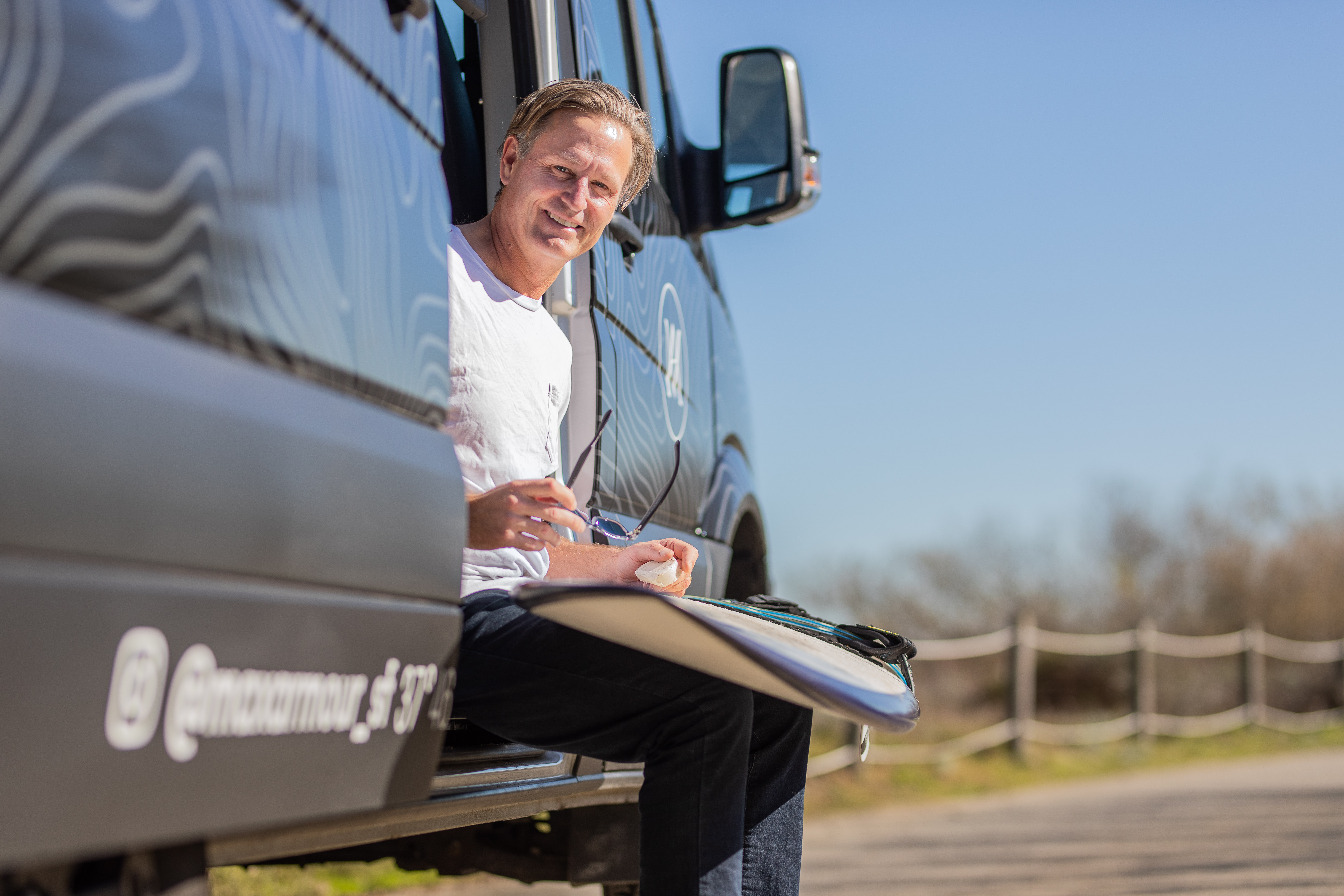 Surfer sitting by van with surfboard, relaxed outdoor lifestyle and coastal travel scene