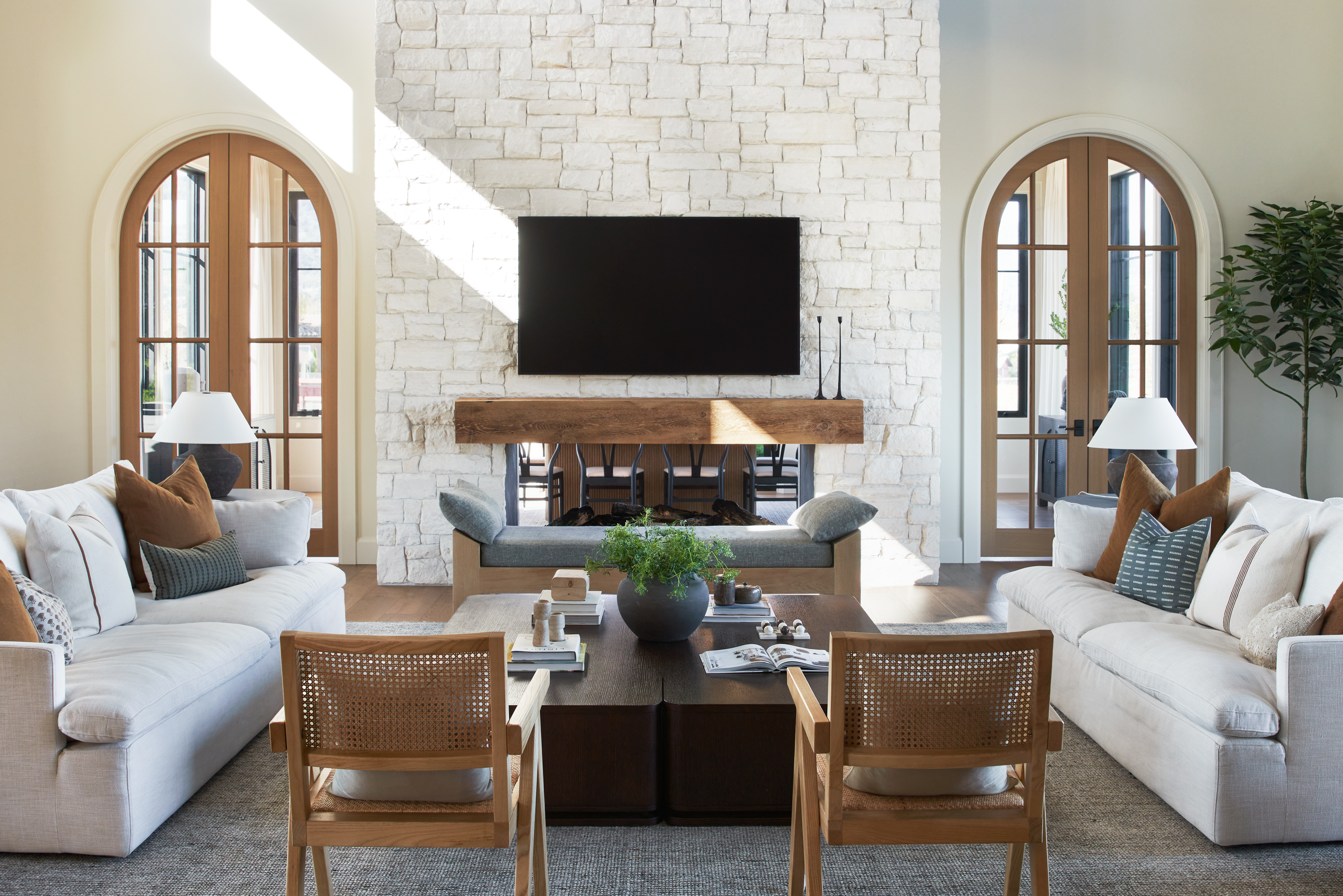 living room real estate photo with sun light, white walls, arched doors, rustic wood and stone fireplace