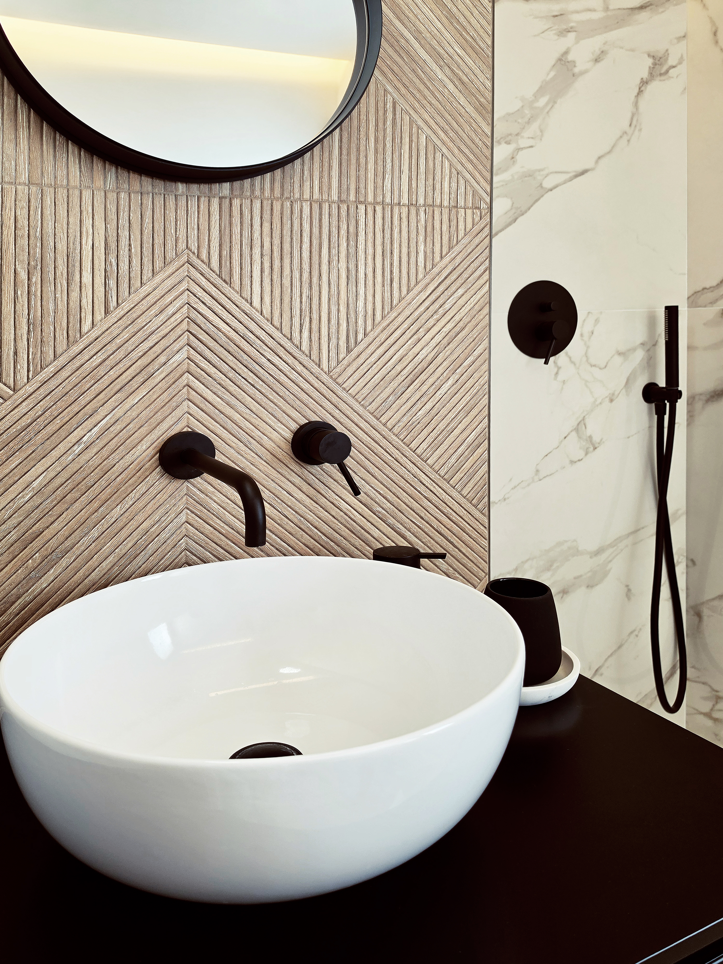 Bagno con ceramica bianca e finiture nere a contrasto su fondo effetto marmo