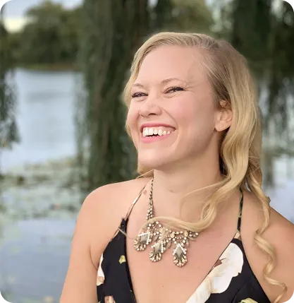 Smiling woman with blonde hair wearing a patterned top and statement necklace