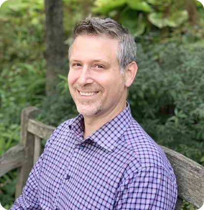 Smiling man in a blue checkered shirt standing outdoors