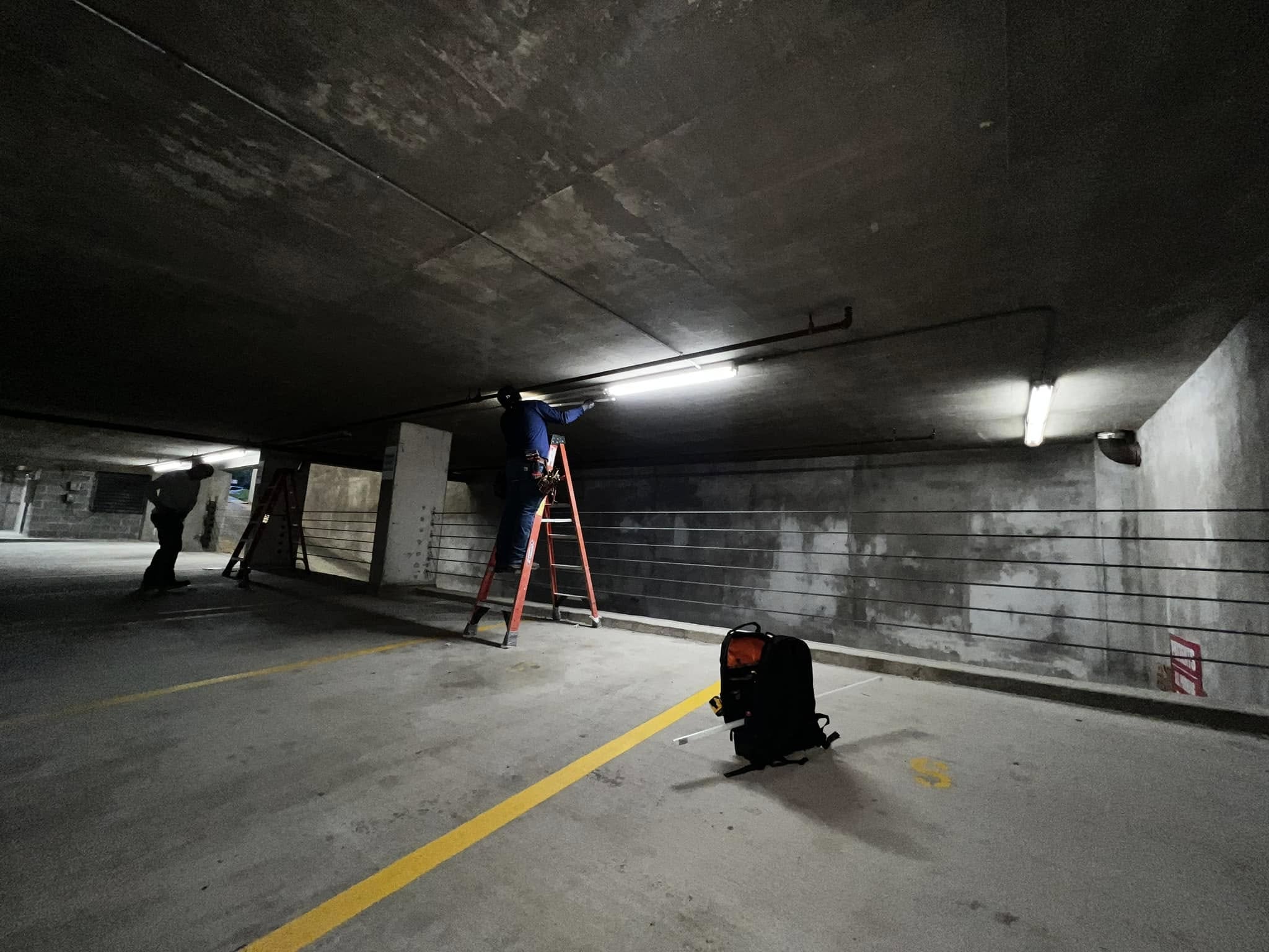 Electrician installing LED lighting in underground parking garage level, Austin TX