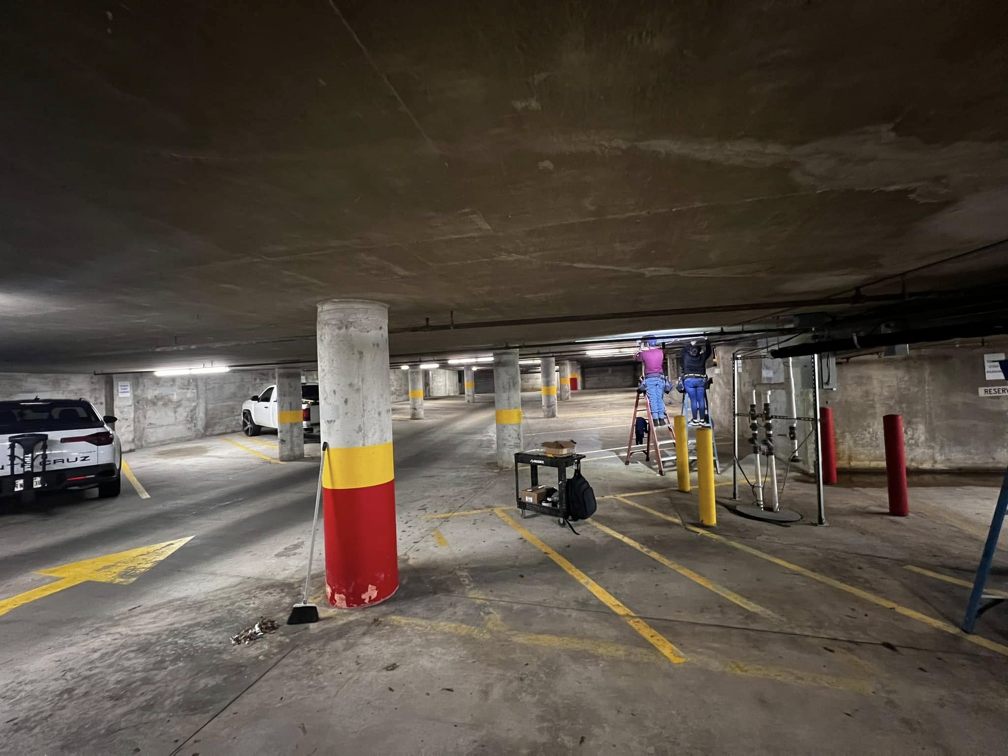 Two electricians installing lighting system in multi-level commercial parking garage, Austin TX