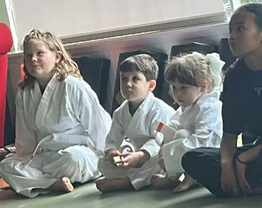 Smiling Asheville kids in martial arts uniforms posing with instructor