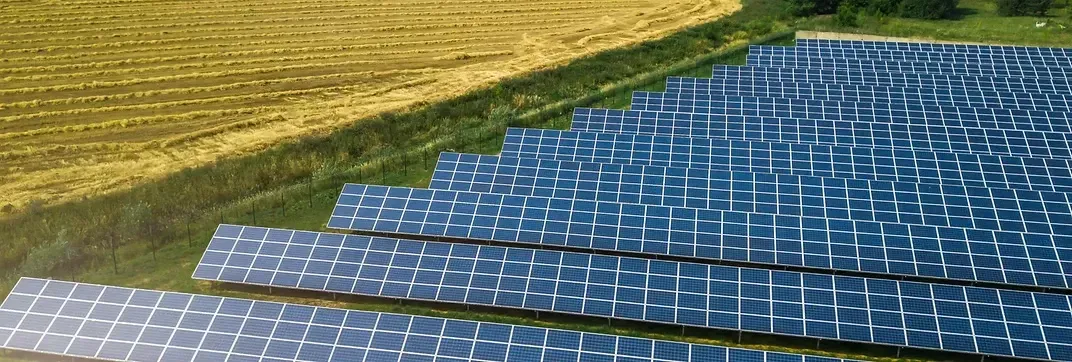 Aerial view of a large solar farm with rows of photovoltaic panels under a clear blue sky.