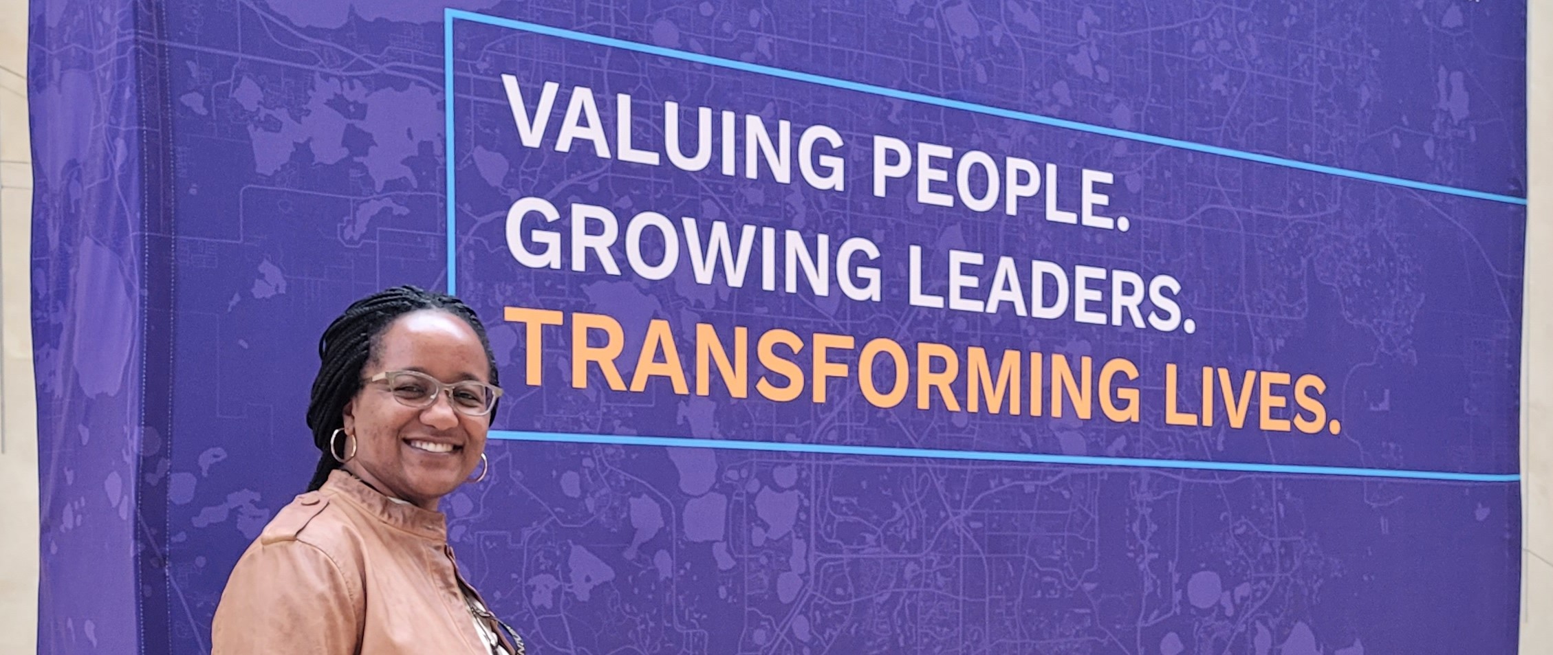 Dr. Heather in front of poster that says, Valuing people. Growing leaders. Transforming lives.
