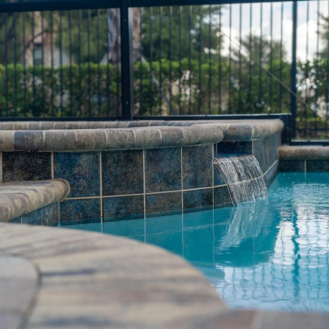 Closeup image of spa waterfall pouring over into swimming pool with palm trees and tropical plants in background