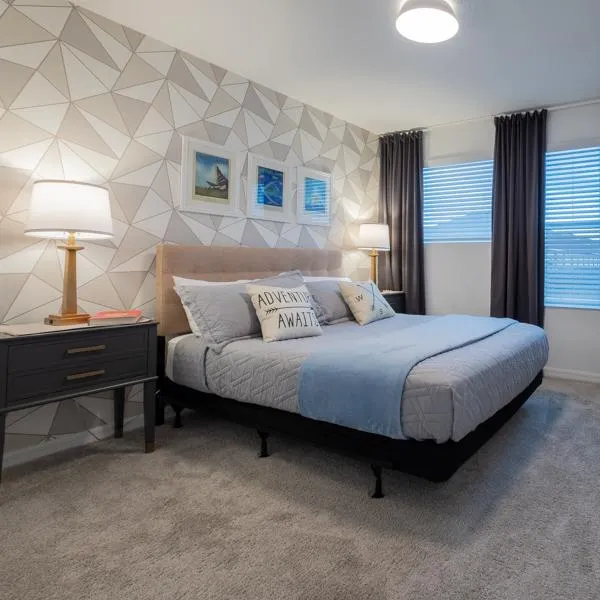 Travel themed bedroom with queen size bed, USB charging bedside lamps, and a brown and gray color scheme. Portraits of imaginary travel destinations hang on the wall.