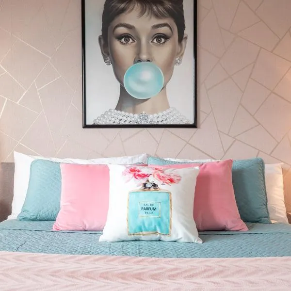 Breakfast at Tiffany's themed bedroom with print of Audrey Hepburn blowing bubblegum, pink wallpaper, and a queen sized bed with blue and pink bedding and decorative throw pillows