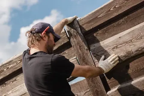 Worker in black t-shirt and black baseball cap securing a wood fence.