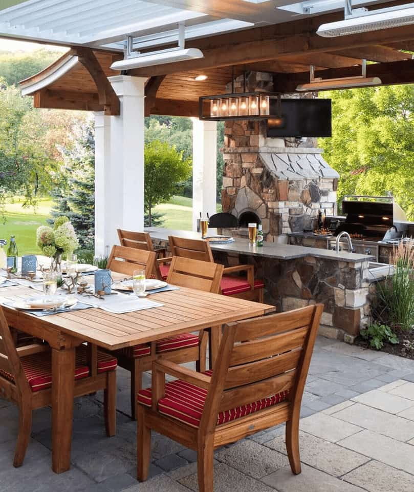 Custom outdoor living space by Decadent Outdoors featuring a motorized StruXure louvered pergola, stone outdoor kitchen with grill and bar seating, stone fireplace, overhead infrared heaters, and dining area in Upstate New York's Capital Region