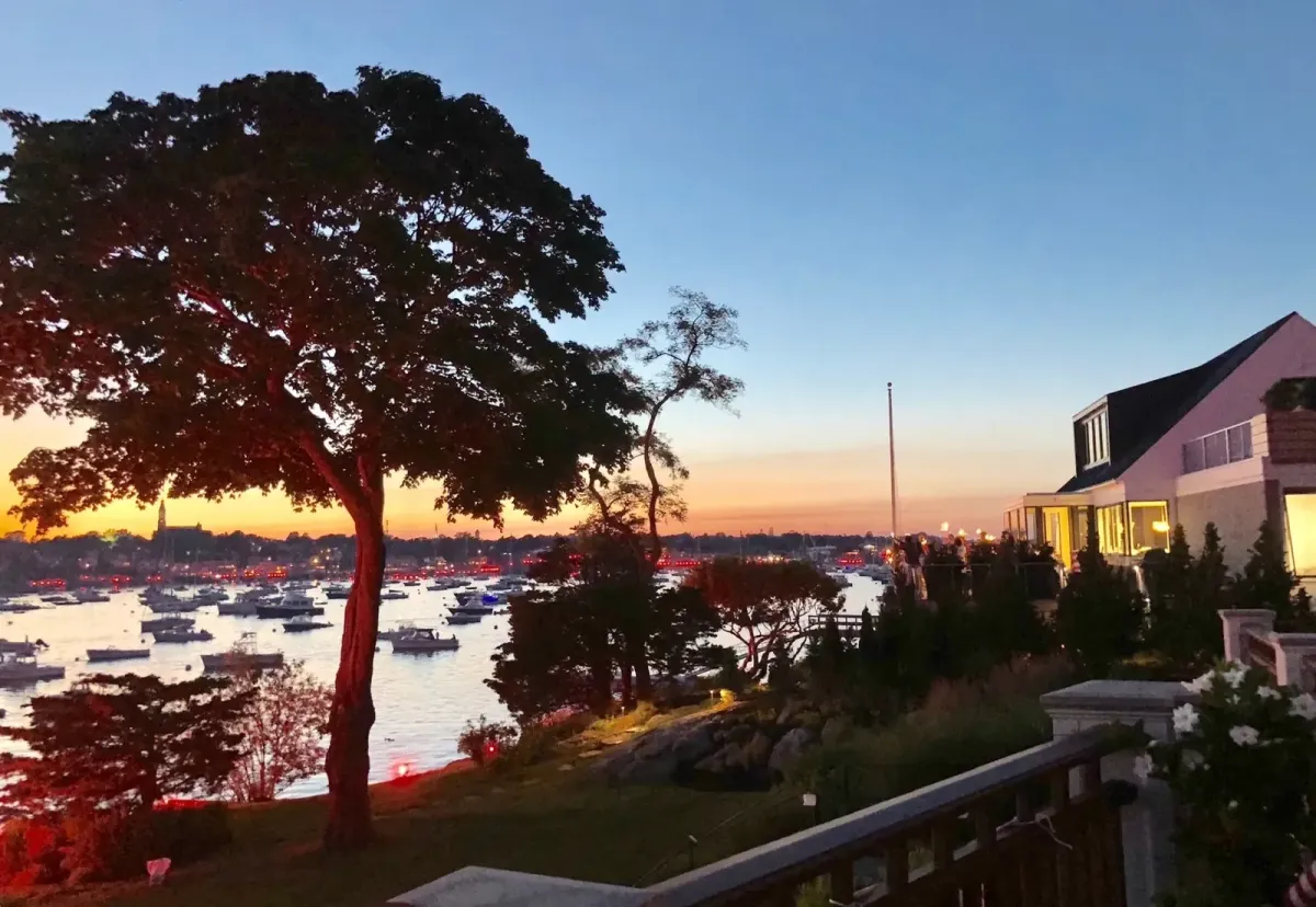 Landscaped waterfront property overlooking Marblehead Harbor at sunset with mature trees, coastal gardens, and boats in Marblehead, MA