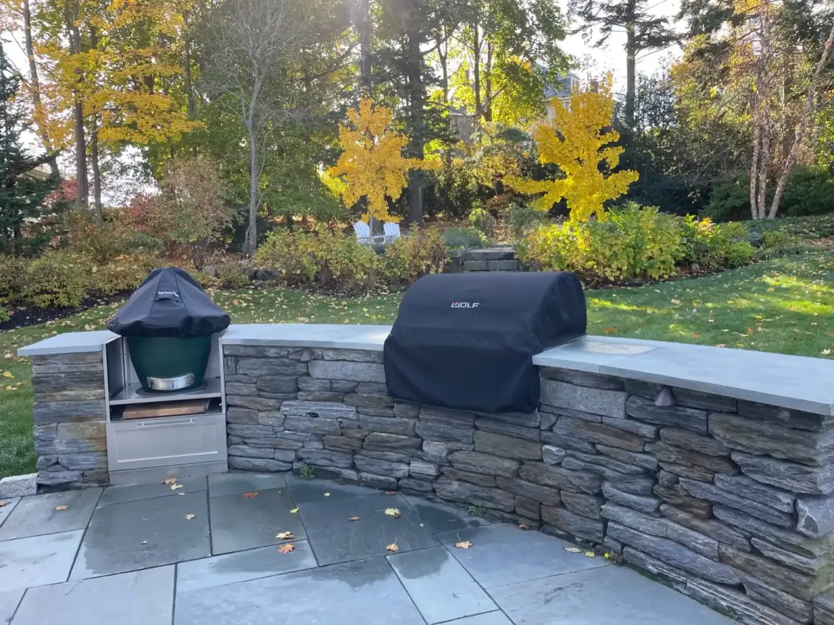 Custom natural stone outdoor kitchen and patio surrounded by fall landscaping in Marblehead, MA