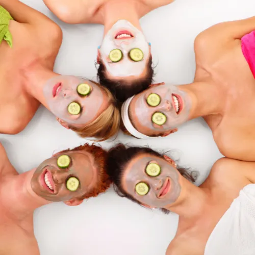 women in circle face up with clay masks and cucumber slices on their eyes for spa party.