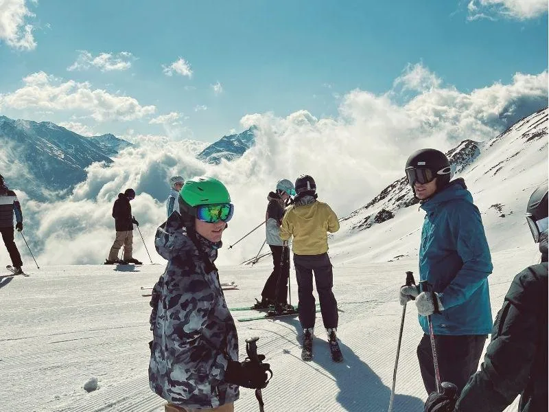 Group of skiers waiting on a snowy slope with beautiful mountains and clouds in the background