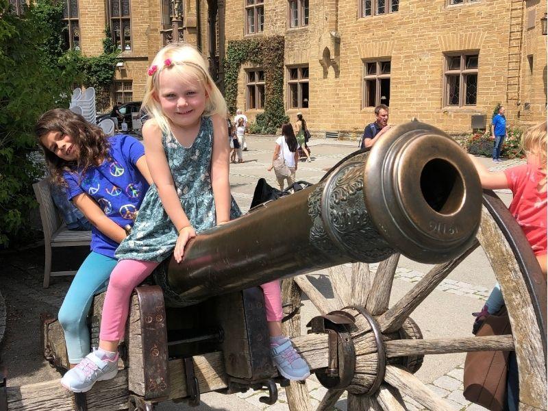 Two kids sitting on an old cannon in a historic castle courtyard in Germany during a family-friendly Europe tour