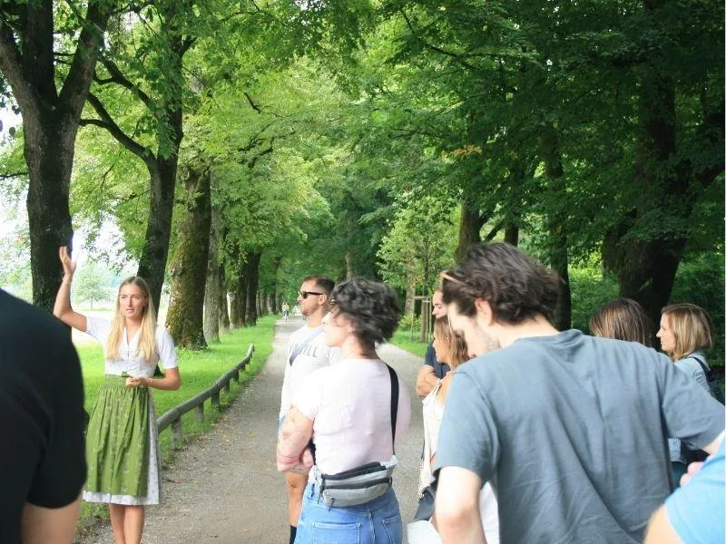 Girl in traditional dirndl walking with a private group along the Hellbrunn allee in Salzburg