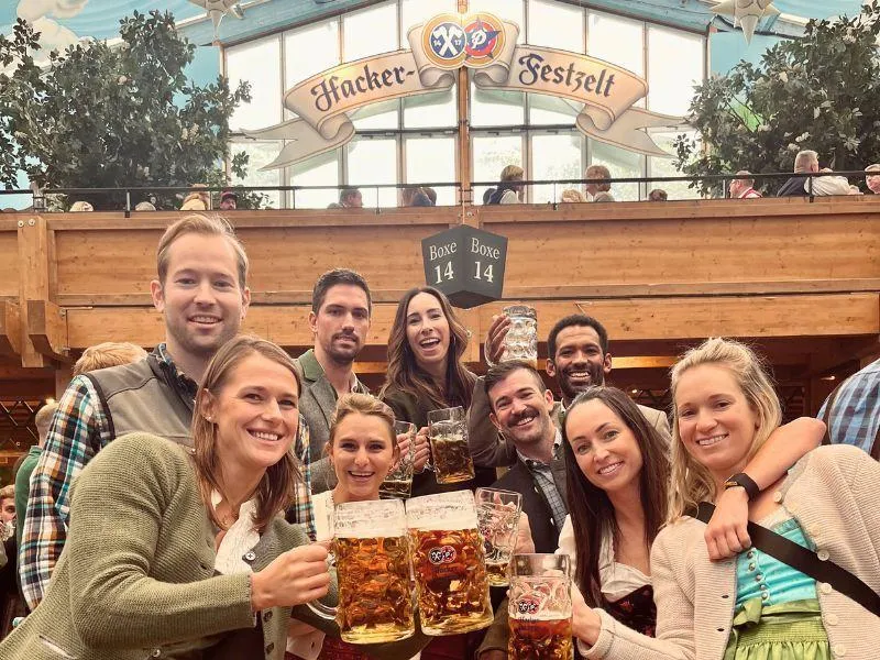 Large group of people inside an Oktoberfest beer tent cheering with traditional steins of beer