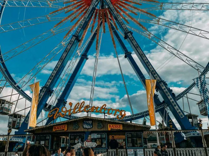 "Riesenrad Ferris wheel at Oktoberfest in Munich with people standing in front of a traditional ticket booth"