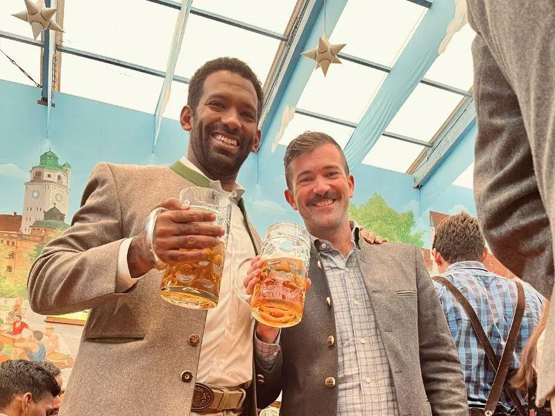 Two men holding large mugs of beer and smiling at Oktoberfest inside a festive beer tent