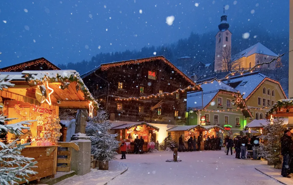 Salzburg Christmas market street with festive stalls, lights, and people walking through Old Town at night
