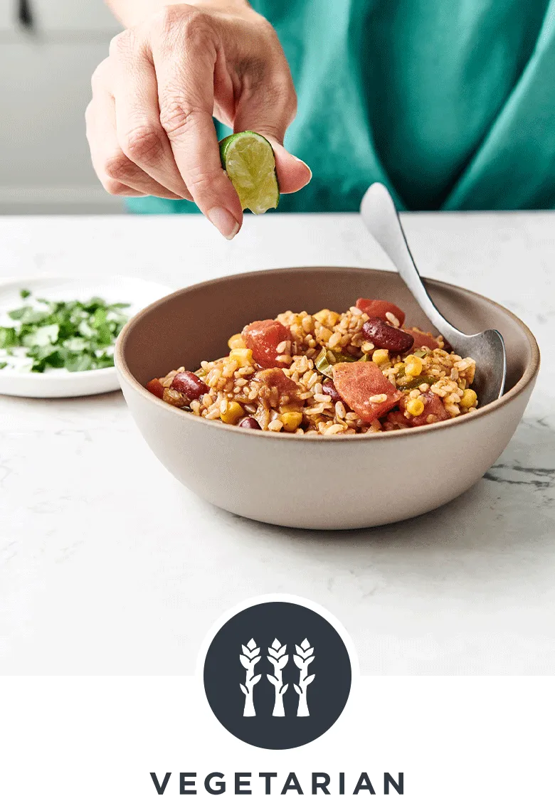 Woman squeezing a lime wedge into a hearty bowl of The Fresh 20 Vegetarian Spanish Instant Pot Crock-Pot recipe