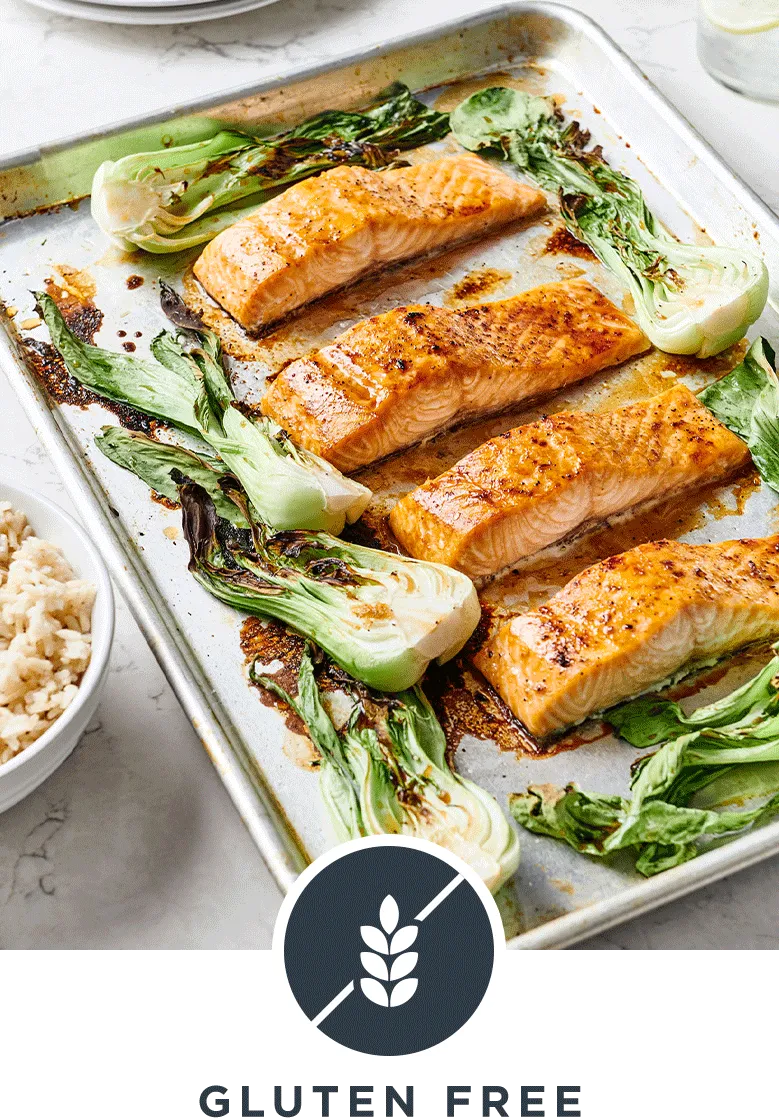 A baking sheet pan loaded with maple soy salmon recipe surrounded with vibrant bok choy and a bowl of rice