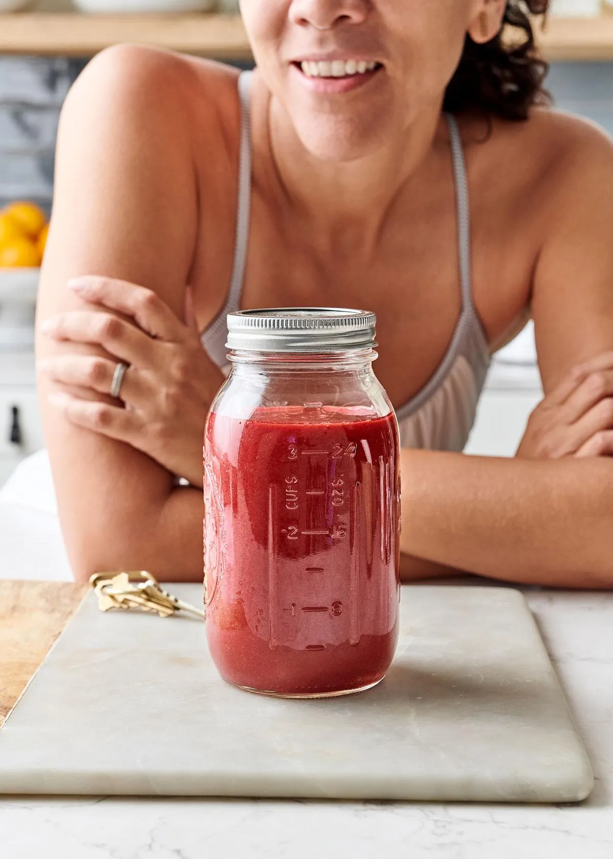 Woman leaning behind a mason jar filled with vibrant pomegranate orange cherry smoothie on a white marble surface