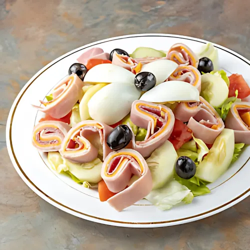 Chef Salad with fresh lettuce, tomatoes, cucumbers, provolone cheese, salami, American cheese, olives, and hard-boiled eggs, offering a hearty, flavorful meal.