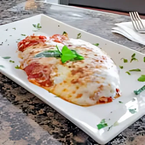 A beautifully plated chicken parmesan with melted cheese and marinara sauce, garnished with fresh herbs.