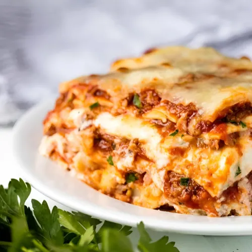 Delicious homemade lasagna layered with pasta, rich meat sauce, creamy ricotta, and melted mozzarella, served on a white plate.