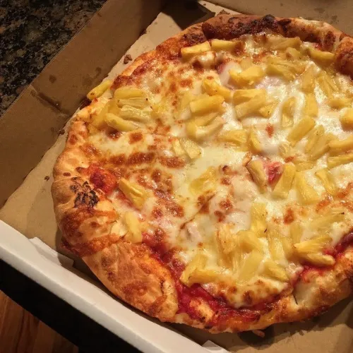 Freshly baked Hawaiian pizza with melted mozzarella, tomato sauce, and sweet pineapple chunks in a takeout box.