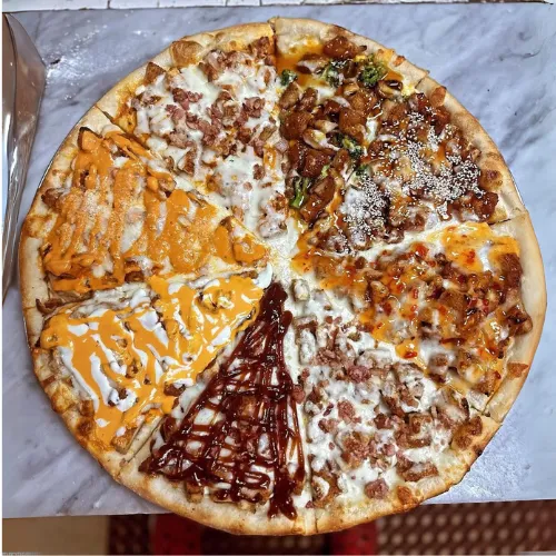 A large pizza divided into six sections, each with different toppings and sauces, placed on a marble surface.