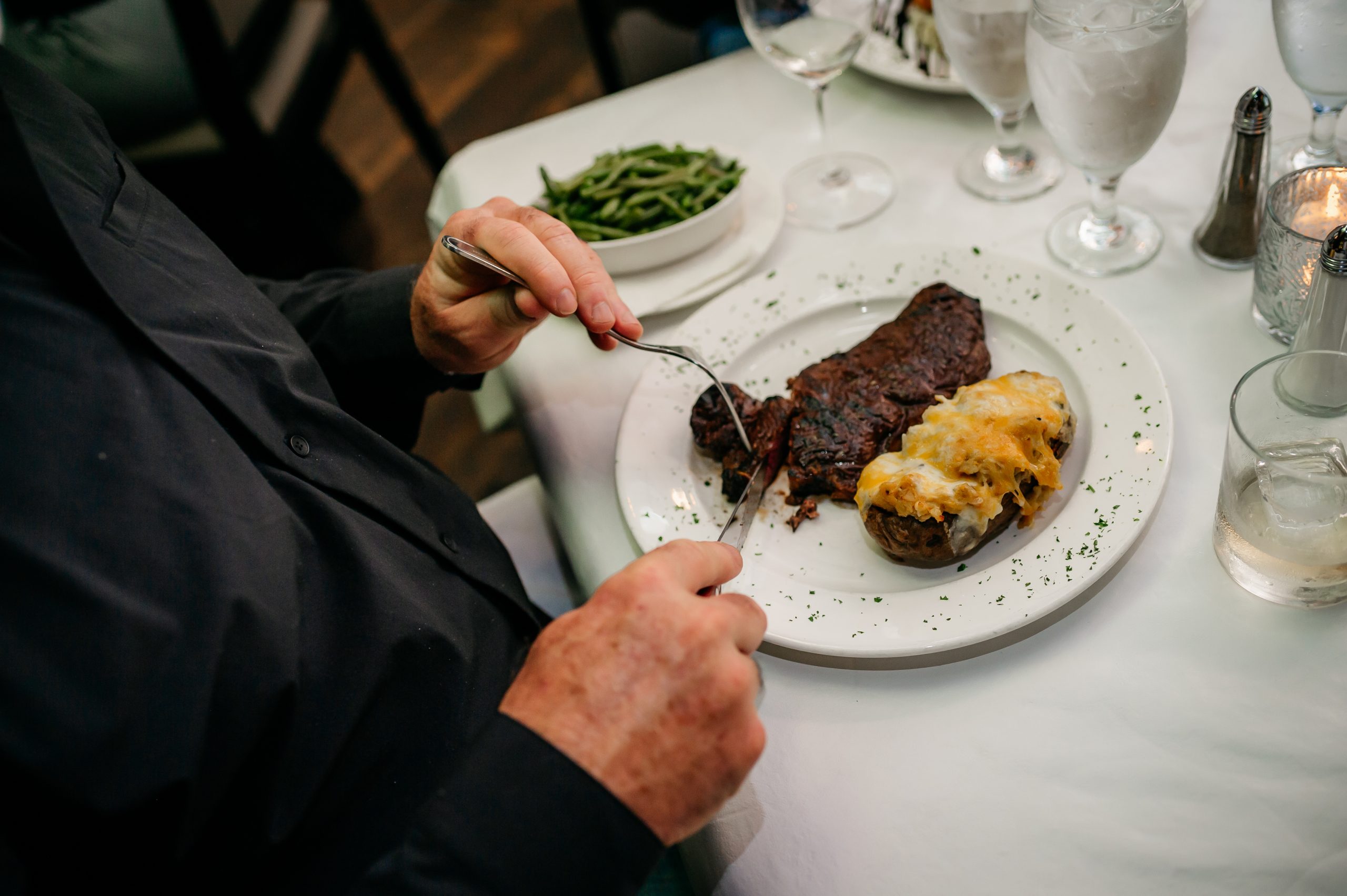 Guest enjoying a hand-cut steak with a loaded baked potato at Epic Chophouse in Kingsley Town Center, Fort Mill, known for fine dining and premium steaks.