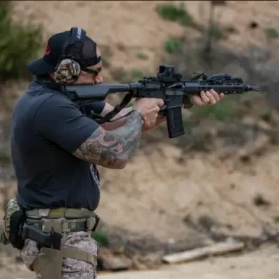 Three adult students receiving pistol fundamentals on a sunlit outdoor lane with a focused instructor demonstrating position and grip.