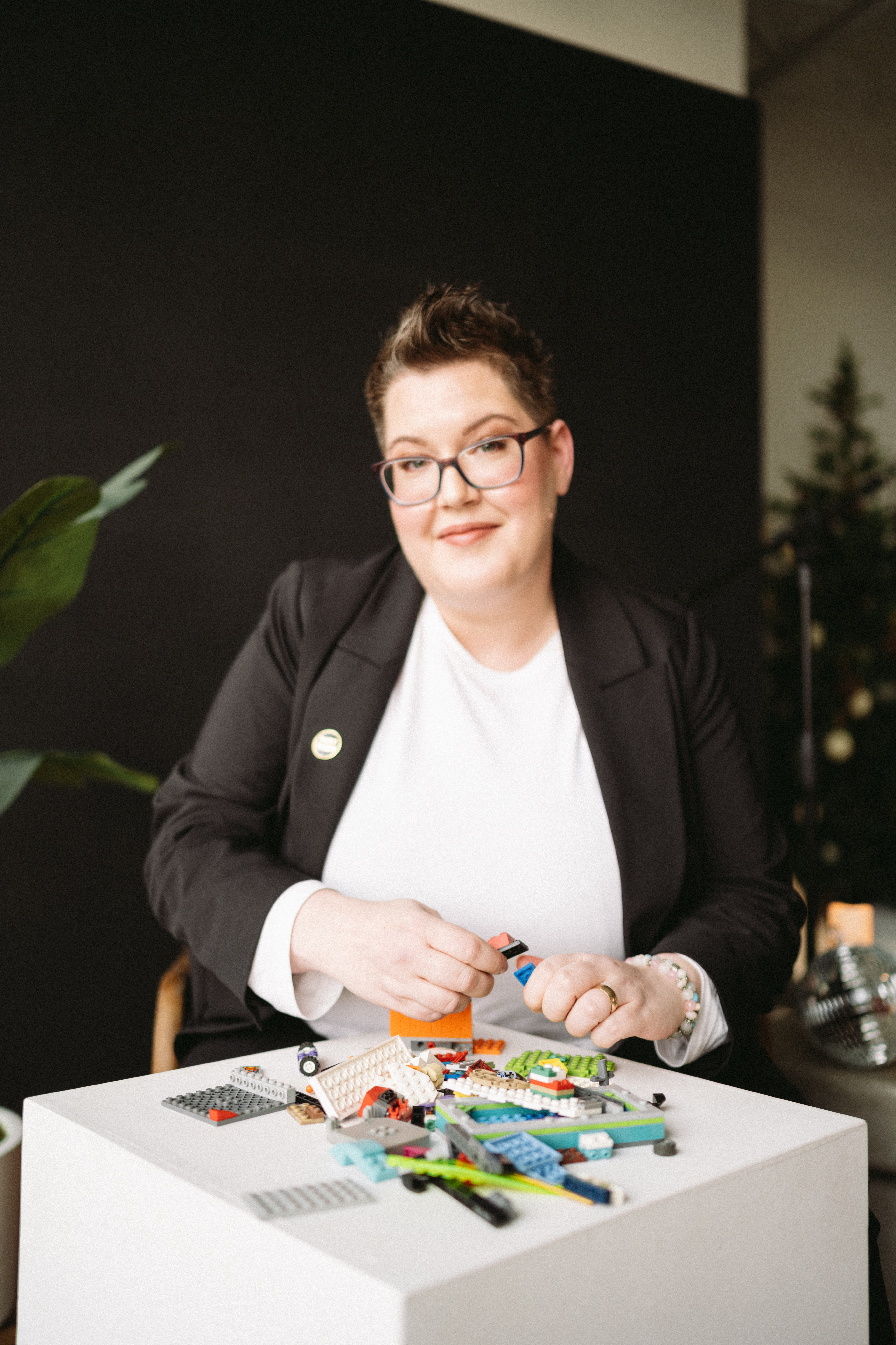Cheryl in a black blazer and white crewneck playing with Lego to regulate their nervous system while being interviewed.