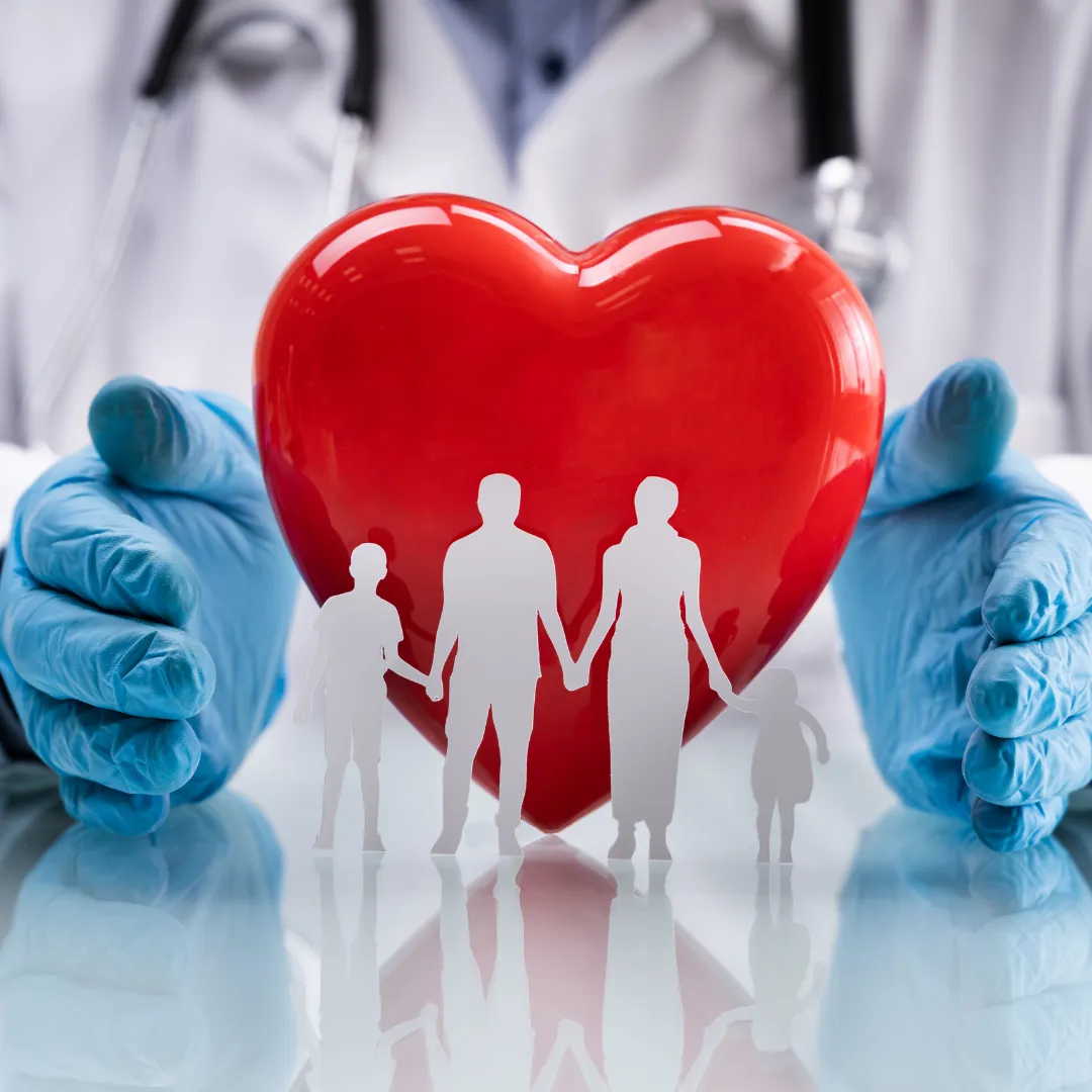 A doctor in scrubs holds a large red heart figurine, surrounded by cut-out family figures representing health and care.